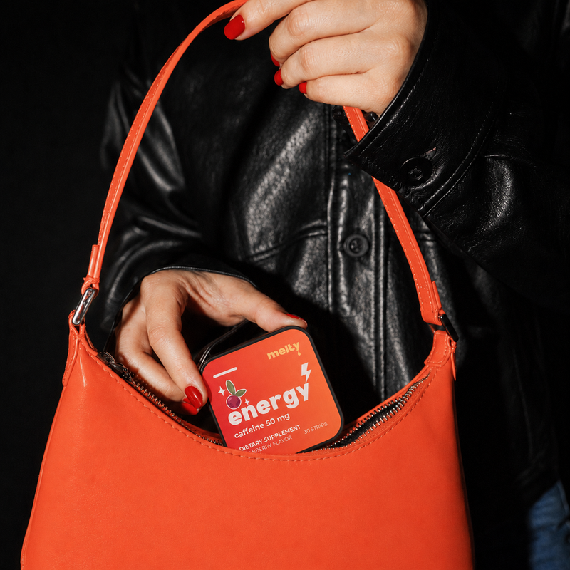 Hand holding melty energy strips container over red handbag