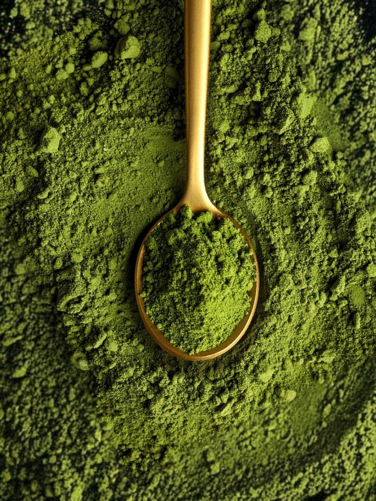 Gold spoon filled with bright green matcha powder on dark surface