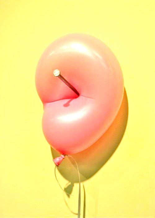 Pink ear-shaped balloon pierced by nail on yellow wall